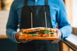 © BONNINSTUDIO/Stocksy - Bartender holding a pastrami sandwich in a small restaurant.