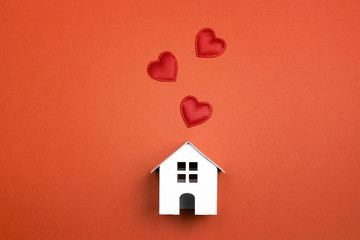 Wall Mural - Miniature white toy house with hearts on red background.