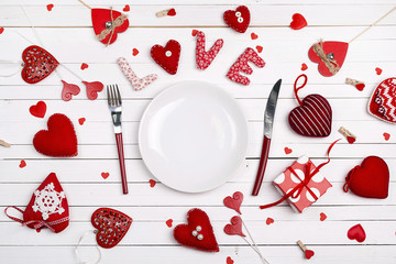 Festive table setting for Valentine's Day with fork, knife and hearts on a white wooden table.  Copy space.