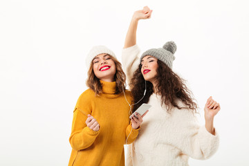 Poster - Two pleased girls in sweaters and hats dancing together