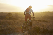 Male Mountain Biker Biking On Moorland Track In Sunlight