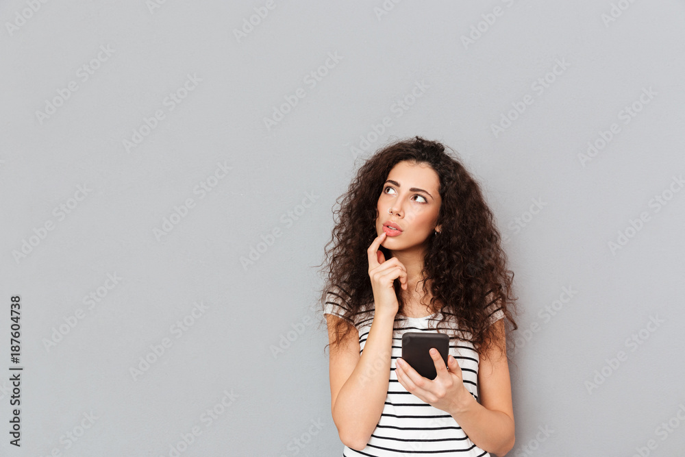 Picture of nice woman touching her lips and looking aside while thinking about something important or trying to remember over grey background - obrazy, fototapety, plakaty 