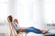 © leszekglasner - Woman at home sitting on modern chair near window relaxing in living room