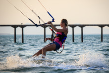 Kite Surfing Girl In Sexy Swimsuit With Kite In Sky On Kiteboard In The Blue Sea Riding Waves Saying Hi. Recreational Activity, Water Sports, Action, Hobby And Fun In Summer Time. Kiteboarding Sunset