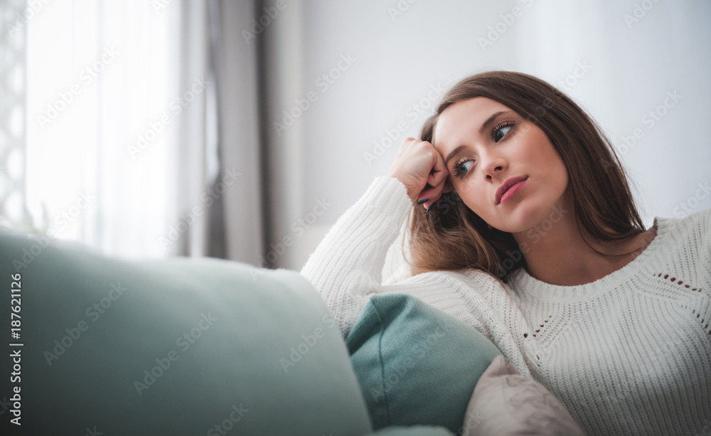 Sad woman sitting on sofa at home deep in thoughts, thinking concept - obrazy, fototapety, plakaty 