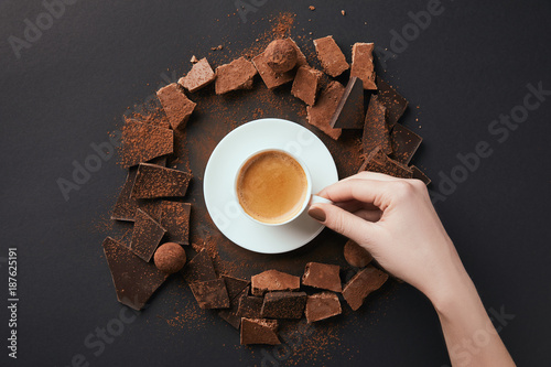 Fotografie, Obraz cropped shot of female hand, cup of coffee, truffles and chocolate on grey surfa