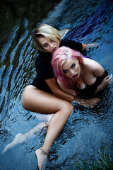 Coveted sexy girls in dresses, passionately pose in the water, embracing each other provocatively and seductively