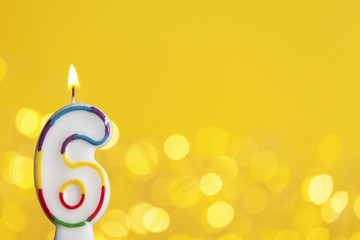 Number 6 birthday celebration candle against a bright lights and yellow background