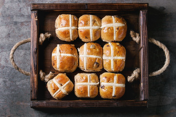 Hot cross buns in wooden tray over old texture metal background. Top view, space. Easter baking.