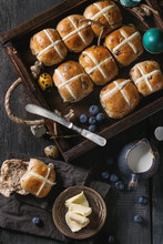 Hot Cross Buns In Wooden Tray Served With Butter, Knife, Blueberries, Easter Eggs, Birch Branch, Jug Of Cream On Textile Napkin Over Old Texture Wood Background. Top View, Space. Easter Baking.