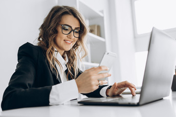 young attractive business woman working in her office with a laptop, looks into the phone and smilin