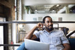 © Cavan Images - Smiling businessman with laptop while sitting on sofa at office