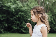 Close-up Of Girl Blowing Dandelion While Standing On Field