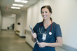 © Cavan Images - Portrait of cheerful female doctor holding laptop computer while standing in hospital lobby