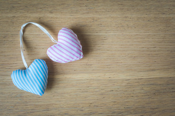 Close up and top view of two, blue and pink, striped textile, fabric hearts bound together on wooden background. Vintage toned. Love, marriage or Happy Valentine's concept