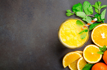 Wall Mural - One glass of freshly pressed orange juice with a straw and mint leaves on a dark black stone background. Top view, horizontal image