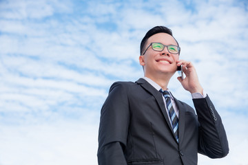 Wall Mural - Young asian businessman in black suit talking with someone via smart phone