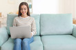 © Africa Studio - Young woman with modern laptop sitting on sofa at home