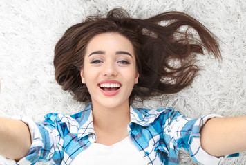 Wall Mural - Beautiful smiling woman taking selfie while lying on carpet at home