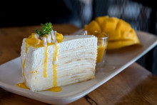Mango Crepe Cake Topped With Mango Sauce On The Table, Blurred Background