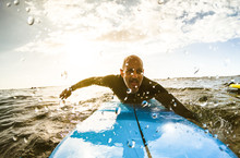 Surfer Guy Paddling With Surfboard At Sunset In Tenerife With Unrecognizable People At Surf Boards On Background - Sport Travel Concept With Shallow Depth Of Field With Drops On Lens As Composition