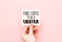 Minimal Composition On A Pale Pink Pastel Background With Girl's Hand Holding Card With Quote "today I Choose To Be A Unicorn" Written In Calligraphy Style