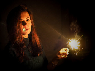 Brunette woman in a sweater lights the Sparkler on Christmas near the Christmas tree