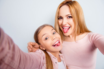 Wall Mural - Self portrait of crazy, foolish mother and doughter showing tongue out, kid making selfie on mobile phone over grey background, spending weekend, woman's day together