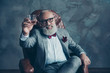 © deagreez - Portrait of bearded, lucky, old rich man in formal wear with bow tie and pocket square, sitting on chair, holding, raise glass with whiskey,  crypto-currency, shares, stock