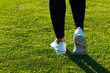 Sports Legs of young athletic woman in dark tights and light sneakers stay or walking along path among dense green grass in training. Copy space. Healthy lifestyle concept. European female