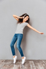 Poster - Full size view of amazing lady in striped t-shirt and jeans wearing headphones dancing and playing around while listening sounds over grey background