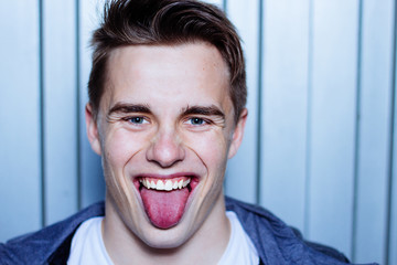 Close up portrait of a young man showing his tongue. Metallic garage door background.