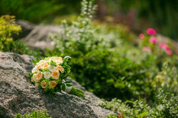 Wall Mural - Wedding bouquet of flowers and greenery with ribbon lies on a rock on a background of greenery. Wedding decorations.