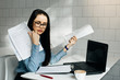 © mnelen.com - girl in glasses sits behind laptop and drinks coffee and looks at documents