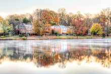 Sunrise On Braddock Lake In Burke, Virginia, USA, Fairfax County With Reflection Of Townhouses, Fog, Mist On Water Surface In Autumn And Orange Trees