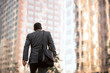 Business man walking to work, motivational conceptual perspective from behind with buildings and copy space