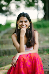 Wall Mural - Portrait of young Indian woman smiling and sitting in a park (Fort Canning Park in Singapore) in the day. She is attractive and is dressed in a summer outfit.