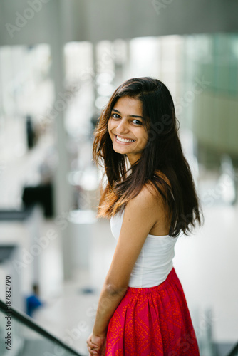 portrait of young indian asian lady going down an escalator she is smiling and looking back over her shoulder and is dressed causally in a summer outfit buy this stock photo
