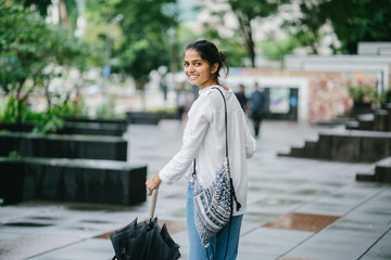 Wall Mural - Young Indian woman walking while holding an umbrella and coffee cup in the city