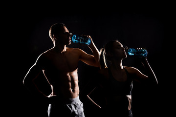 silhouettes of athletic young couple drinking from bottles isolated on black