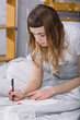 © LIGHTFIELD STUDIOS - girl writing something to notebook in bed in morning
