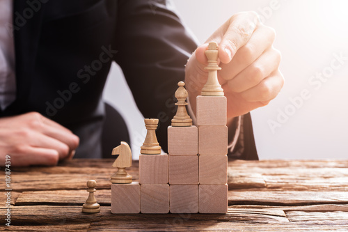 Fotografie, Obraz Businessperson Arranging Chess Piece On Wooden Blocks