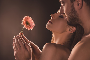 naked sensual lovers holding flower, on brown