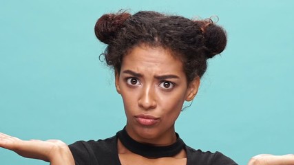 Wall Mural - Close up view of funny african woman in t-shirt covering her face and showing grimaces over blue background