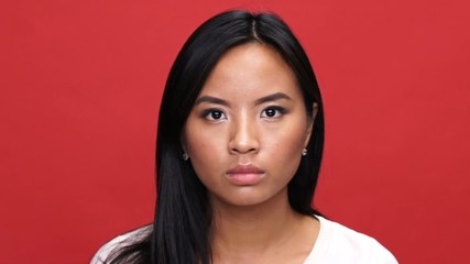 Sticker - Close up view of displeased asian woman in t-shirt looking around over red background