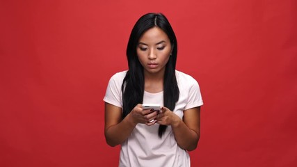 Sticker - Displeased asian woman in t-shirt writing message on smartphone over red background