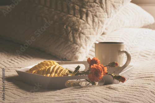 Plakat Taca z kawą, kwiatem i ciastkiem z jabłkiem, leży na miękkiej nakładce na łóżku.