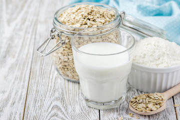 Healthy oat products, flakes, milk and flour in glass jars on white background. Selective focus, space for text.