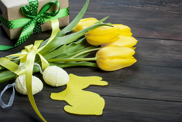 Wall Mural - bouquet of yellow tulips and chikken easter eggs with a blue ribbon on a wooden background