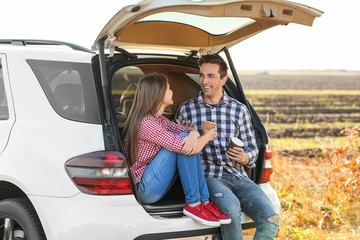 Poster - Beautiful young couple sitting with coffee in car trunk